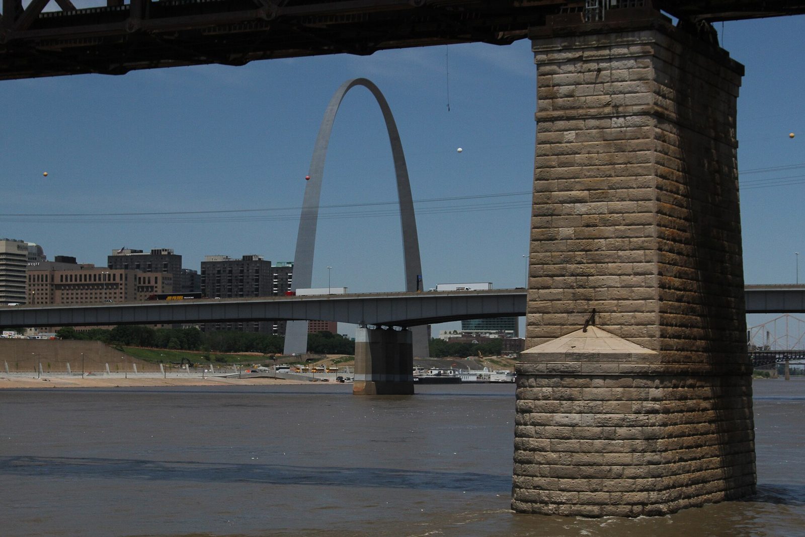 The Gateway Arch framed between the stone pier of the Eads Bridge and the deck of an interstate bridge over the Mississippi